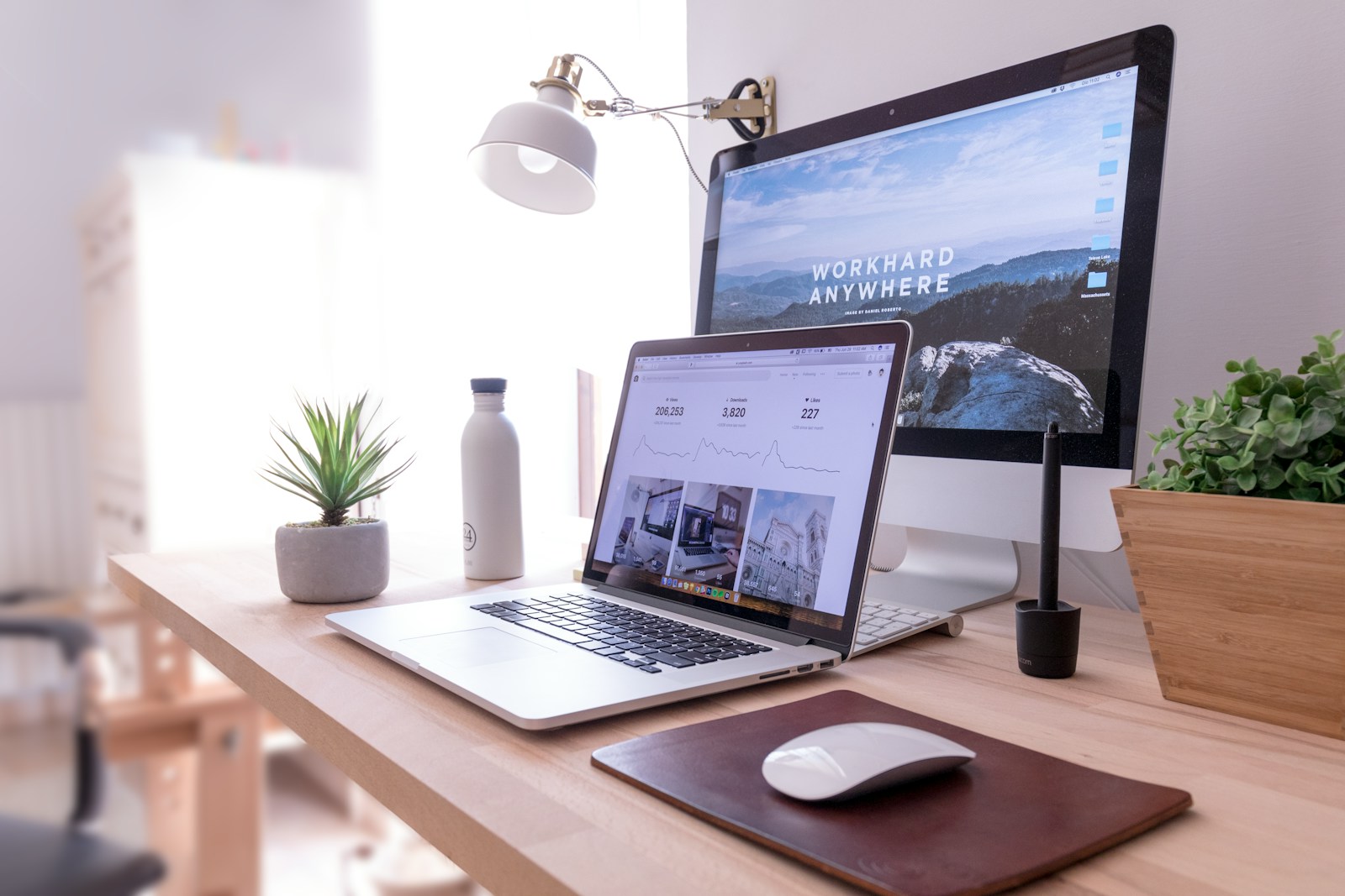 Heller Arbeitsplatz mit Laptop, Bildschirm und Pflanzen